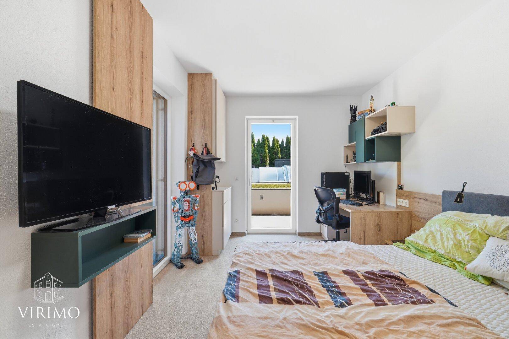 Kinderzimmer mit Teppichboden, Fernseher und Zugang zu einem kleinen Balkon.