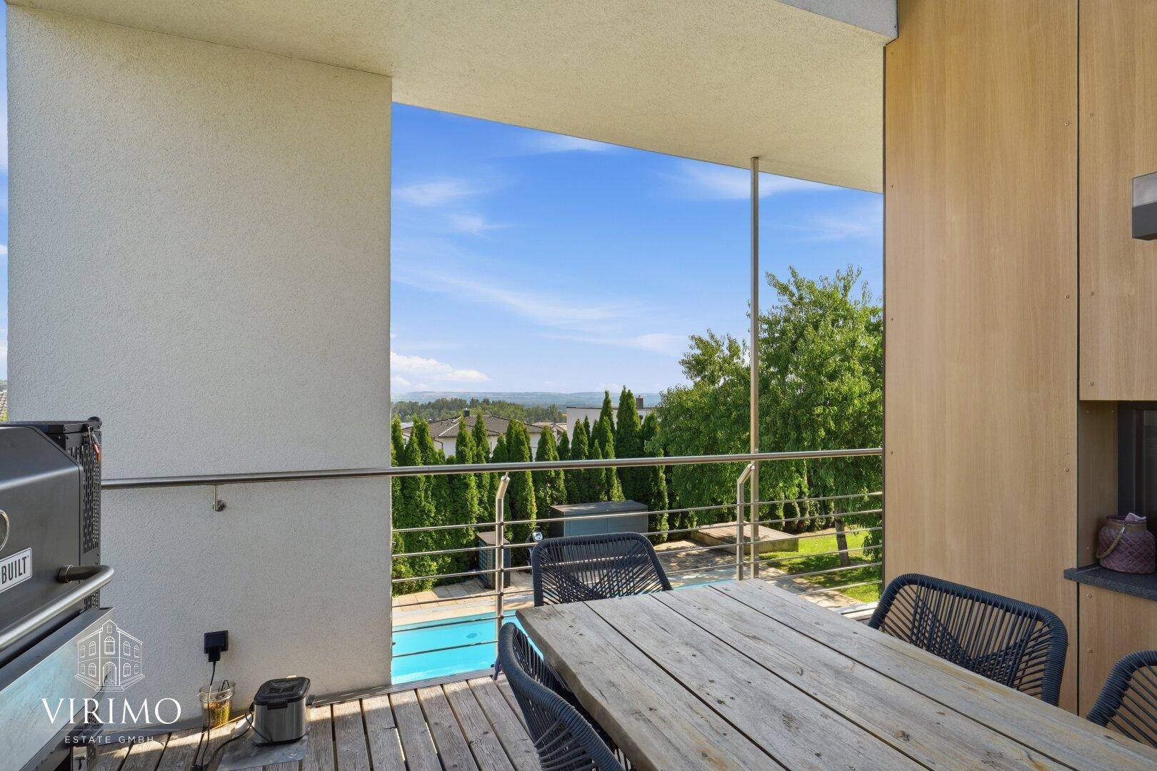 Überdachter Balkon mit Esstisch, Grill und Blick auf den Pool und die Landschaft.