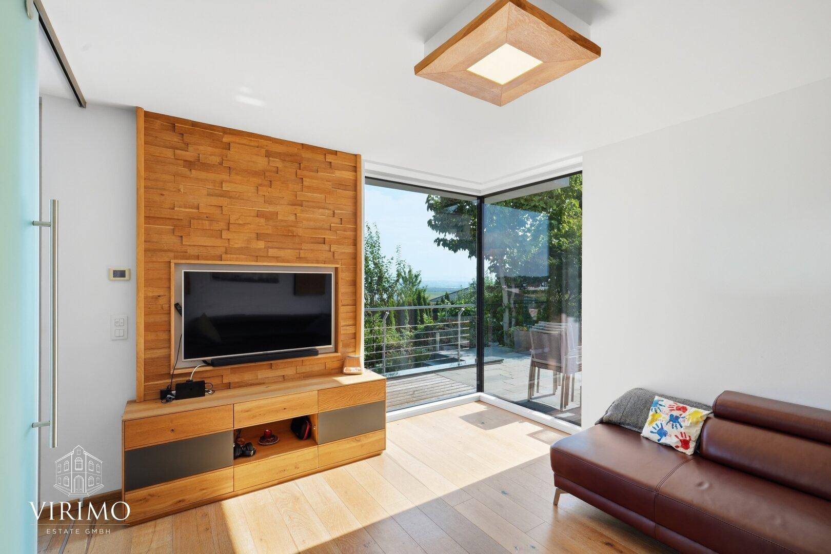 Moderner Wohnbereich mit Holzwandverkleidung, Fernseher und Zugang zum Balkon.