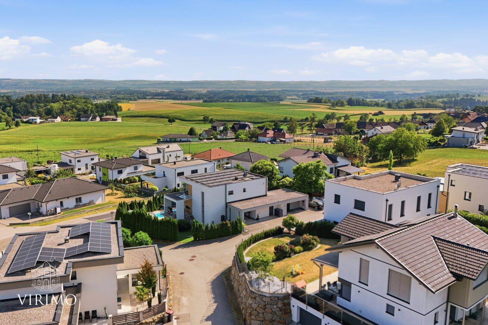 Luftaufnahme einer modernen Wohnsiedlung mit Einfamilienhäusern und weitem Blick über die grüne Landschaft.