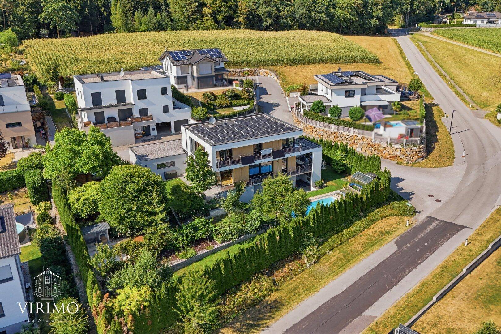 Moderne Villa mit Swimmingpool und Photovoltaikanlage, umgeben von grünen Hecken und Feldern.
