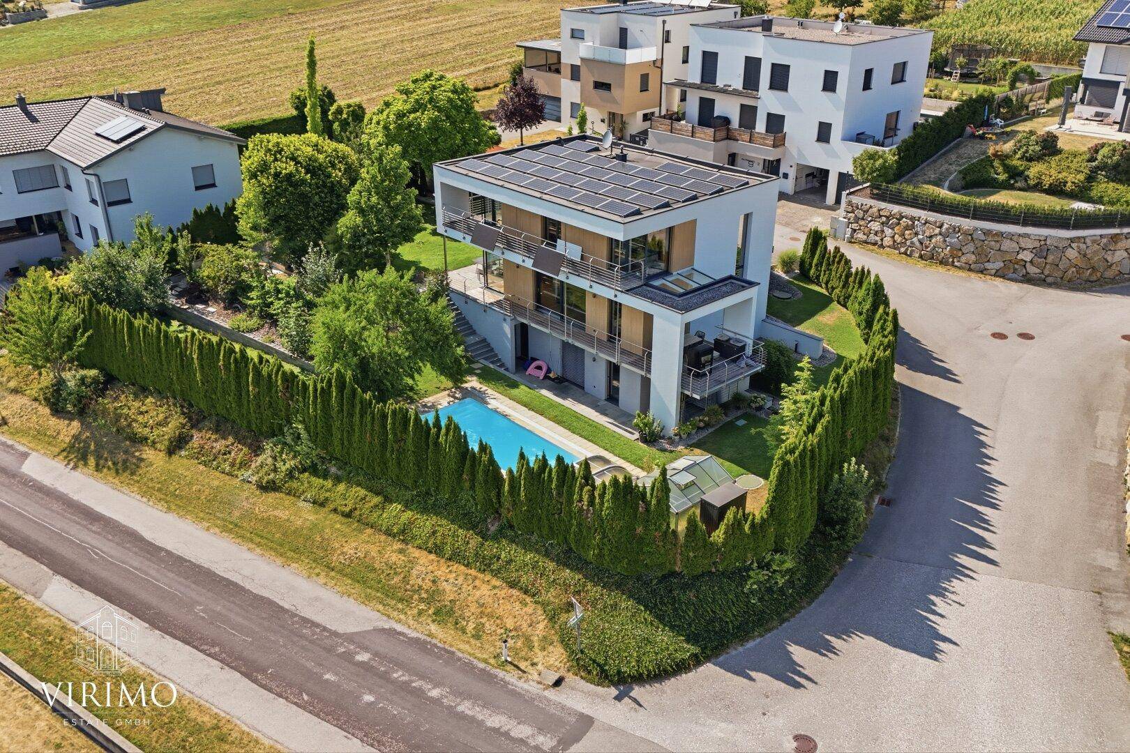 Elegantes modernes Haus mit privatem Pool und Photovoltaikanlage, umgeben von hohen grünen Hecken.