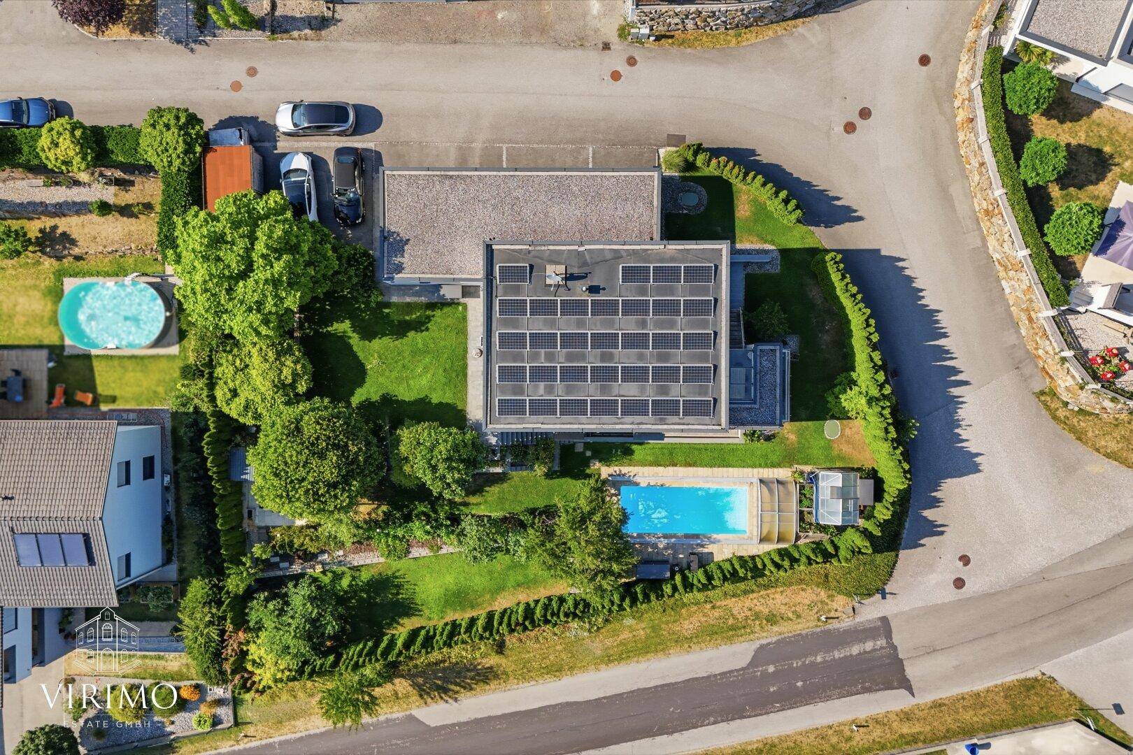 Draufsicht auf das Anwesen mit modernem Haus, Pool, gepflegtem Garten und Photovoltaikanlage auf dem Dach.