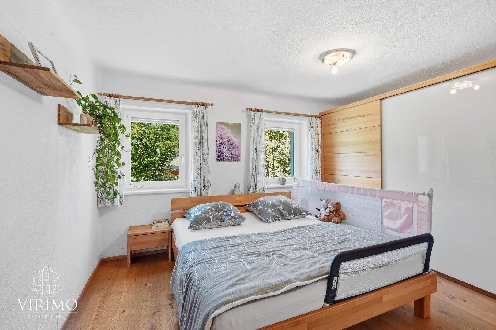 Gemütliches Schlafzimmer mit Holzbett, Einbauschrank und Blick auf die umliegende Natur.