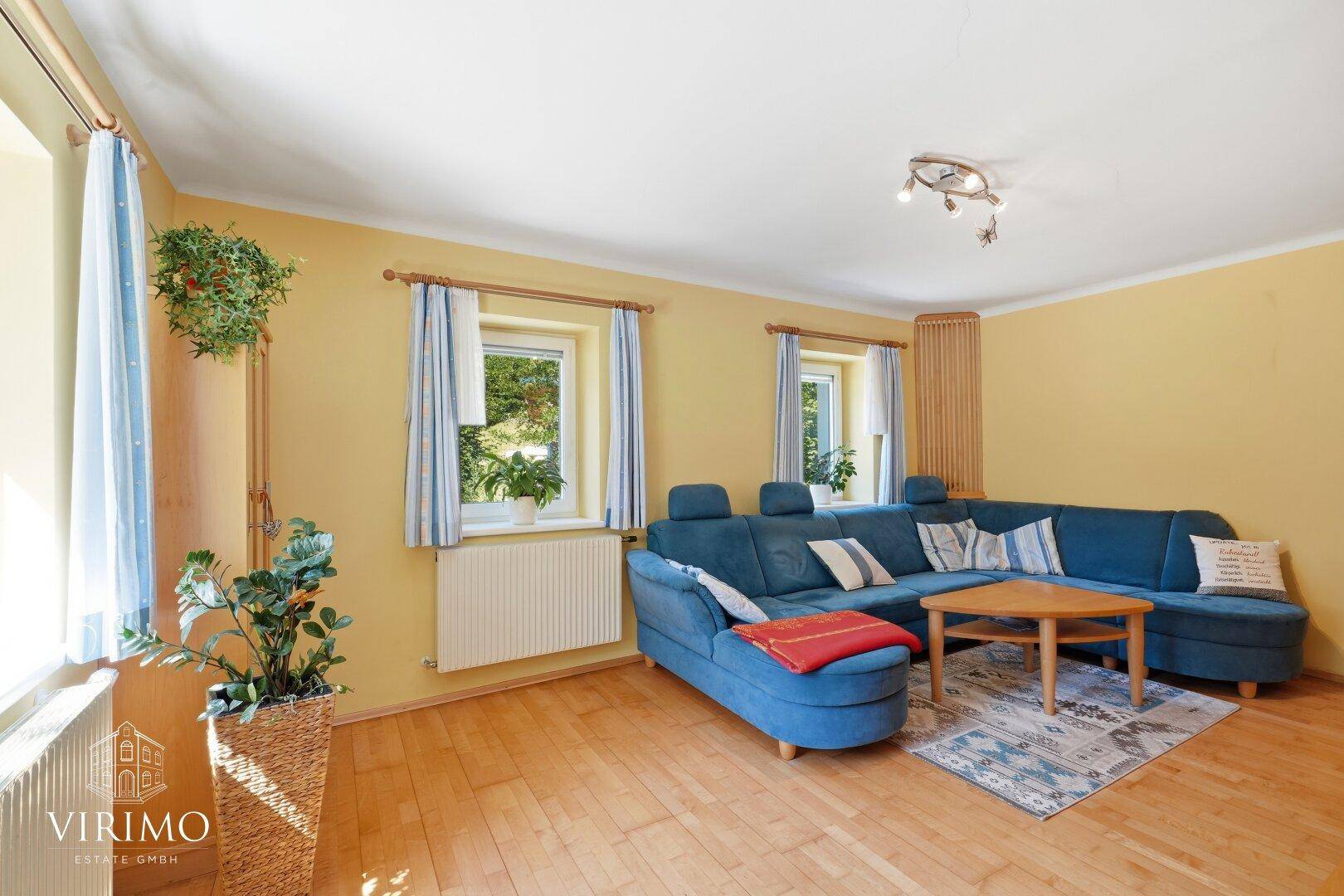 Gemütliches Wohnzimmer mit blauer Eckcouch, gelben Wänden und Holzboden.