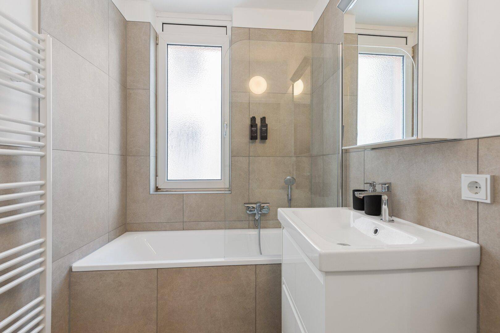 Modernes Badezimmer mit Badewanne, Waschbecken und beheiztem Handtuchhalter.