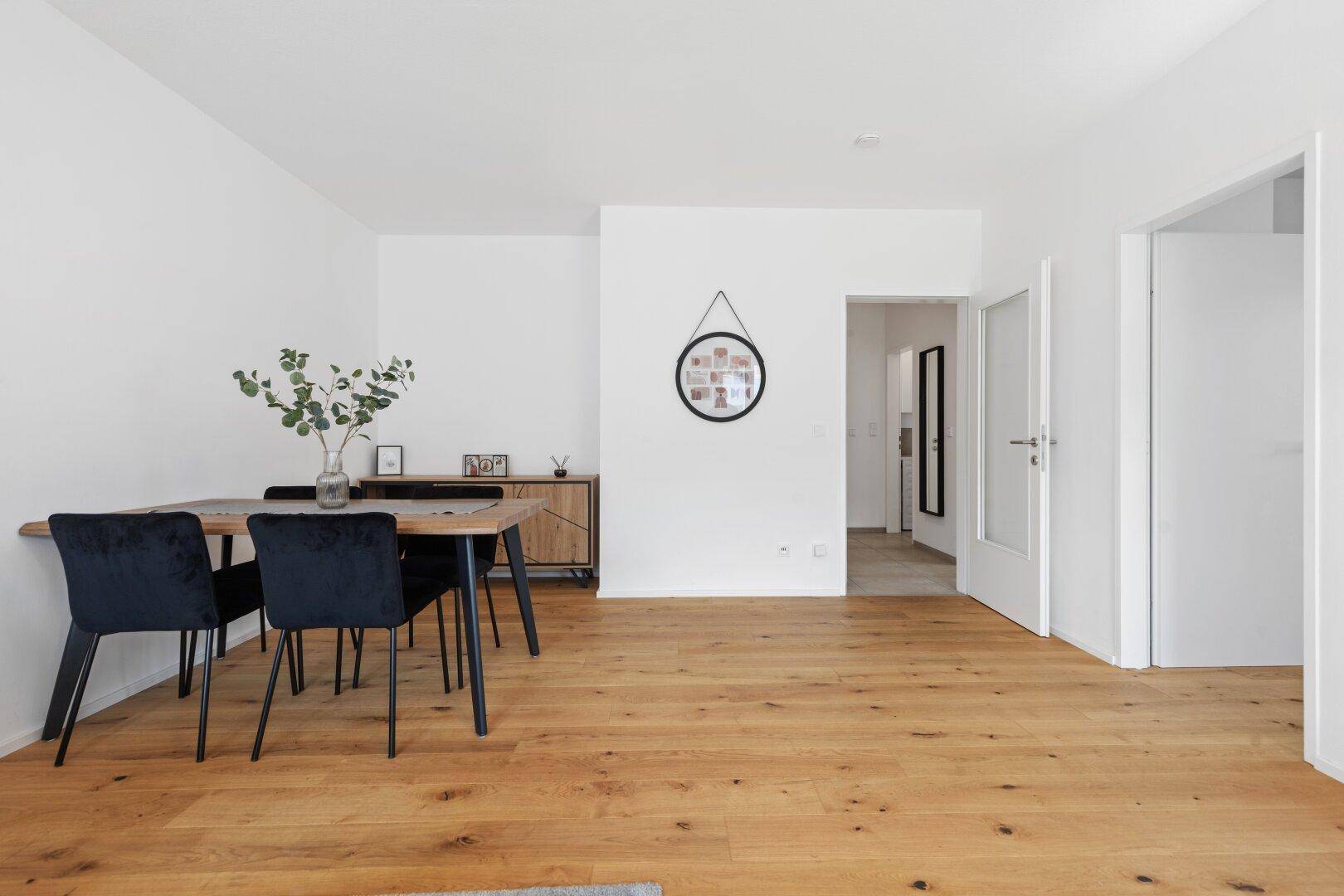 Moderner Essbereich mit Holztisch, schwarzen Stühlen und Holzboden.