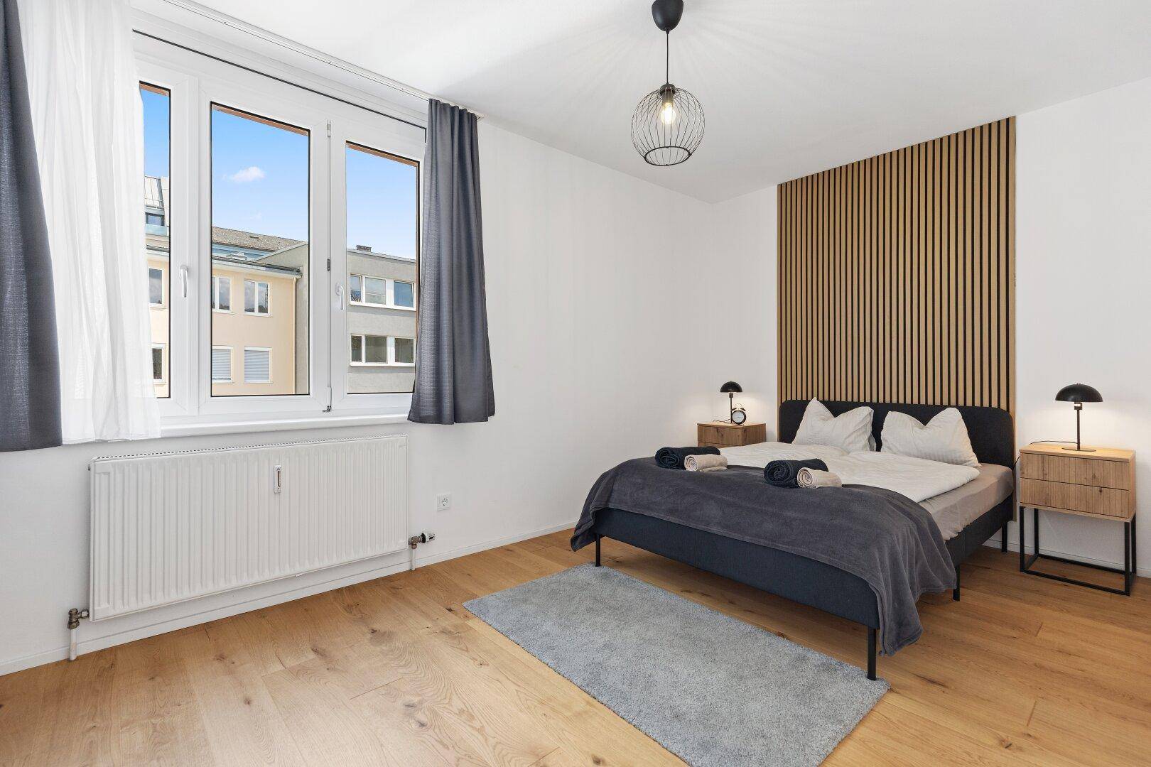 Helles Schlafzimmer mit Doppelbett, Holzboden und Fenster mit Blick nach draußen.