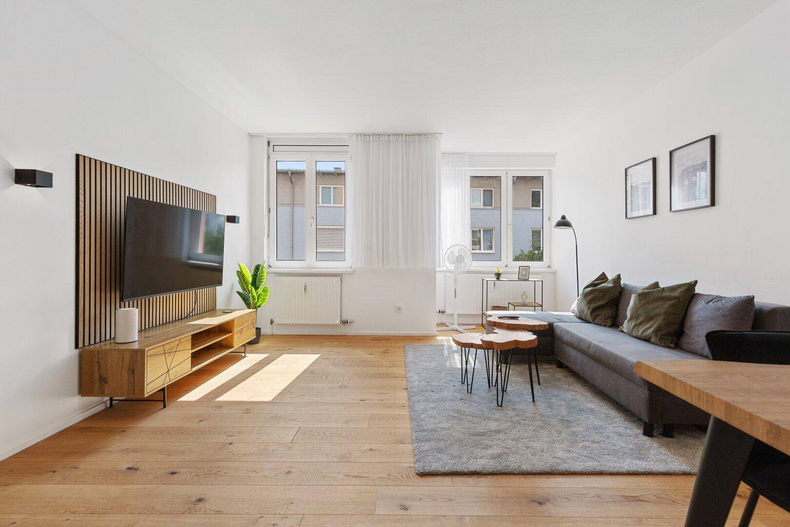 Geräumiges Wohnzimmer mit Holzboden, moderner Einrichtung und viel Tageslicht.