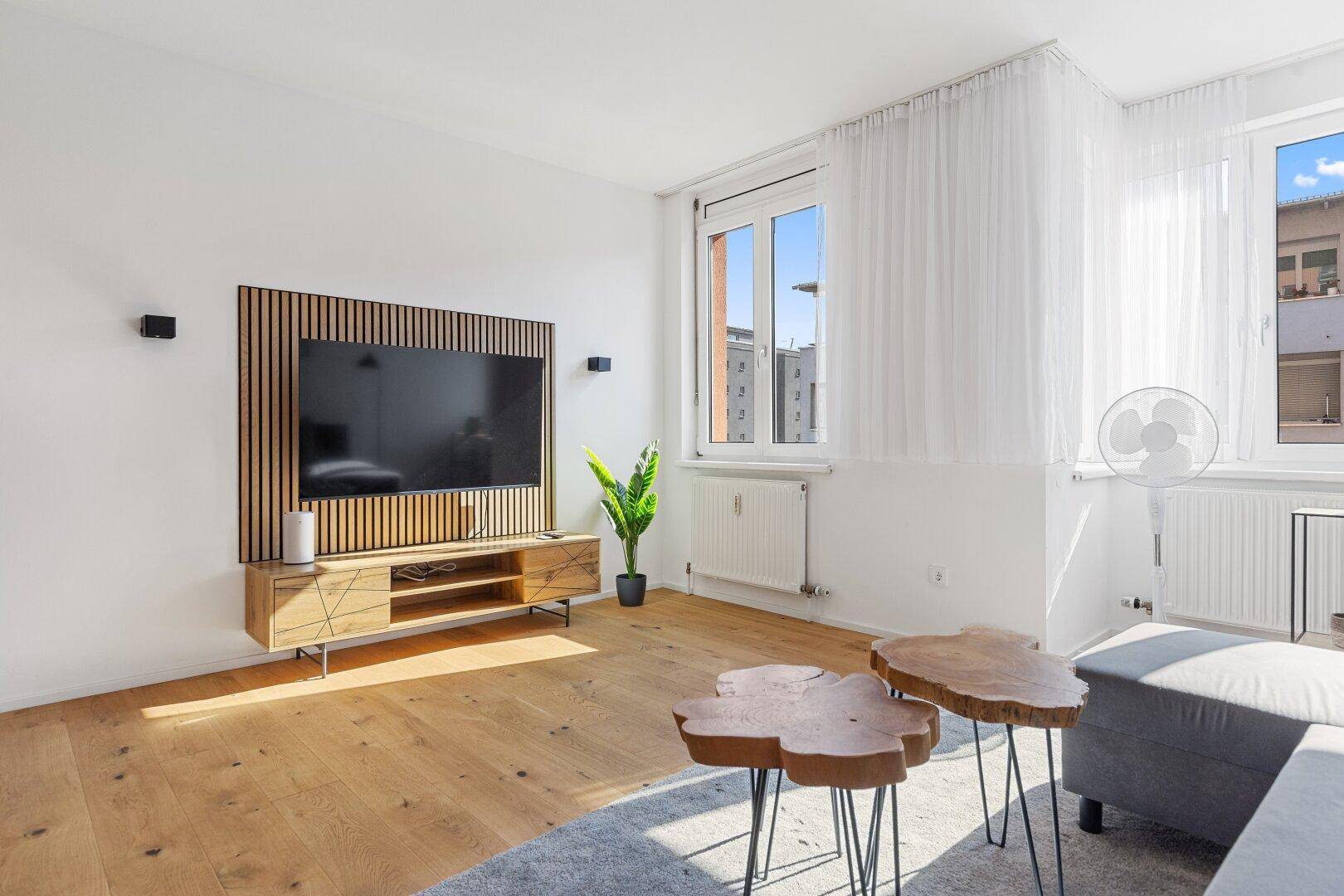 Lichtdurchflutetes Wohnzimmer mit Holzboden, Couch und dekorativen Beistelltischen.