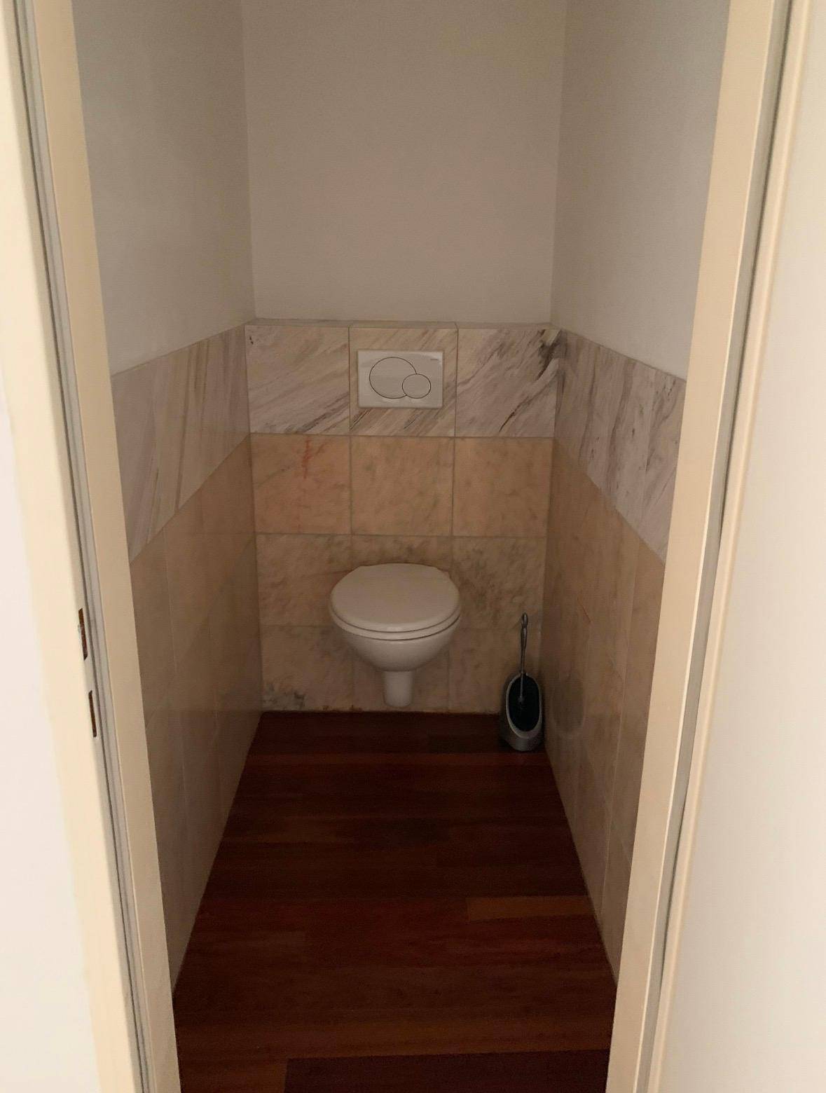 Separate Toilette mit Wand-WC und Fliesen an den Wänden, ausgestattet mit Holzboden.