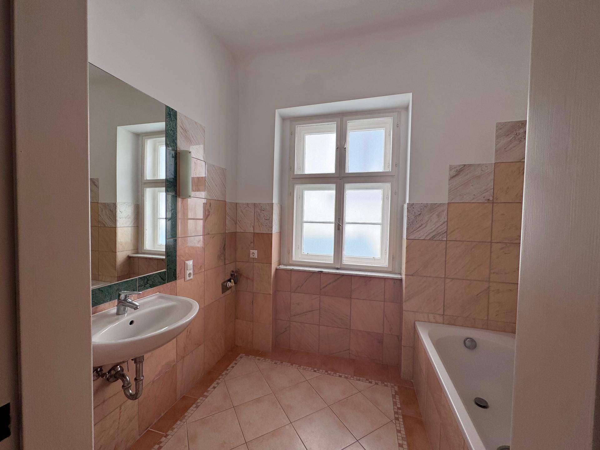 Badezimmer mit Badewanne, Waschbecken und einem Fenster, das für Tageslicht sorgt.
