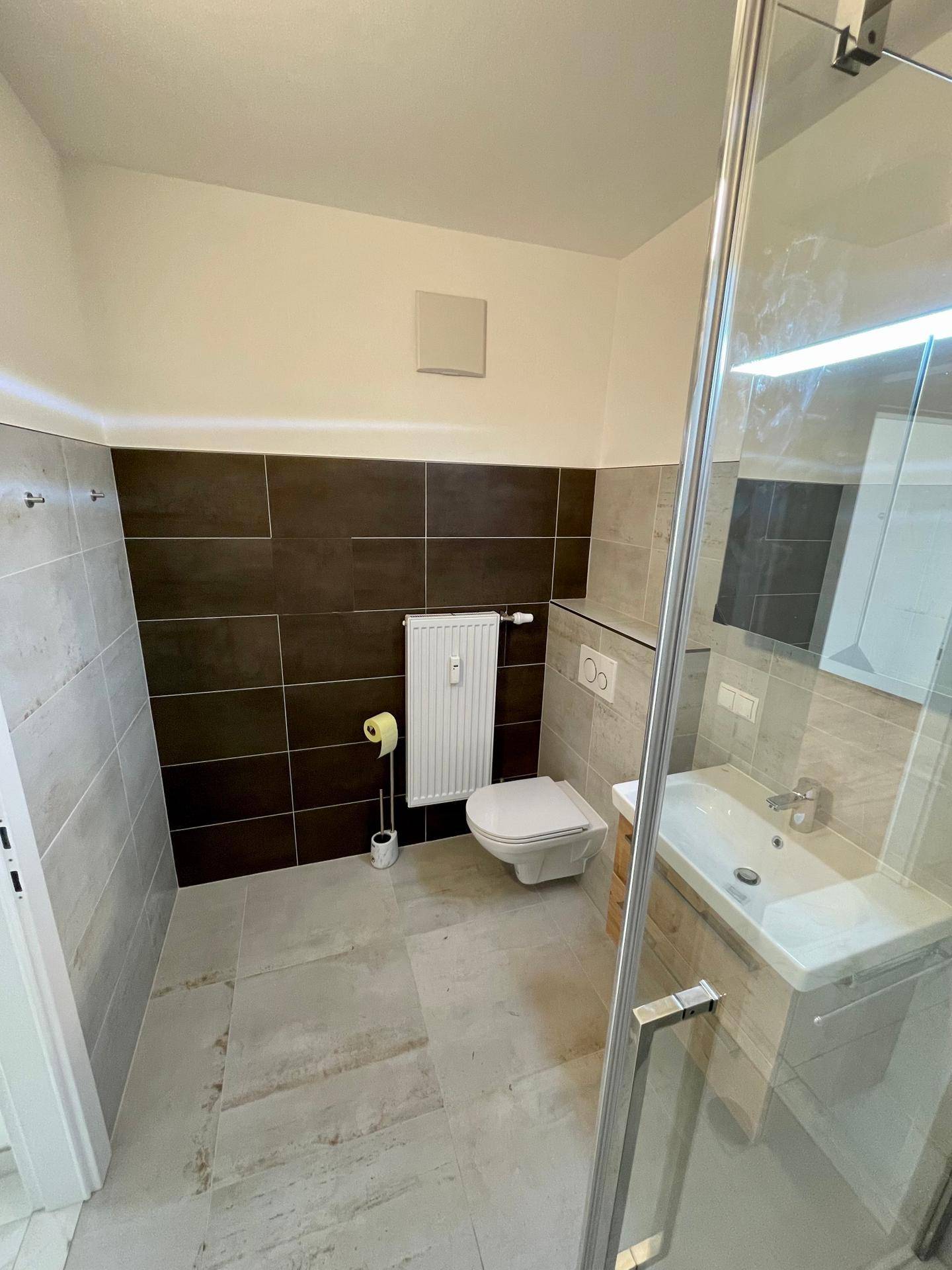 Modernes Badezimmer mit Duschkabine, Wand-WC und stilvollen Fliesen in Grau- und Brauntönen.