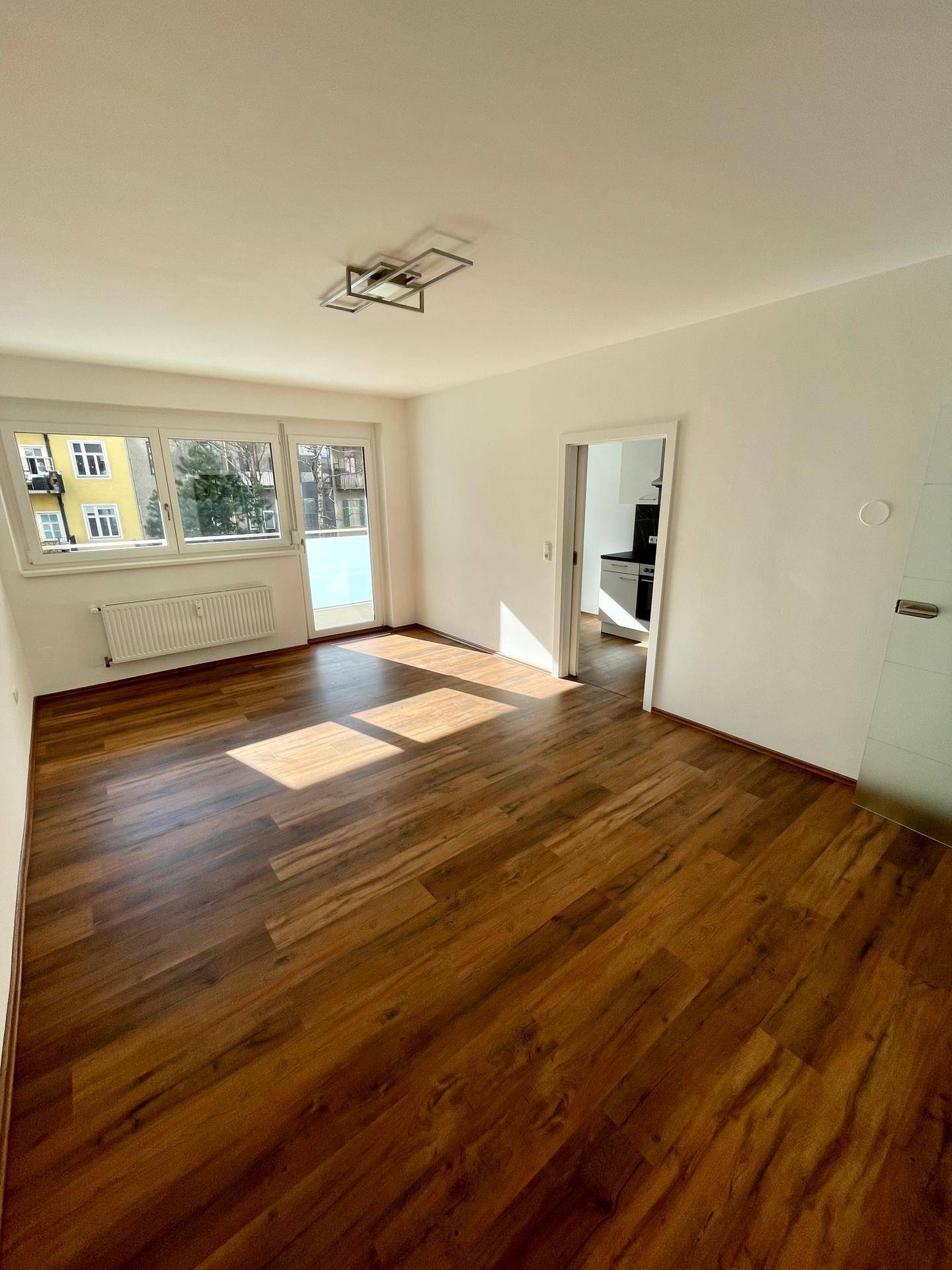 Geräumiges Wohnzimmer mit Holzboden, viel Tageslicht und Zugang zur Küche.