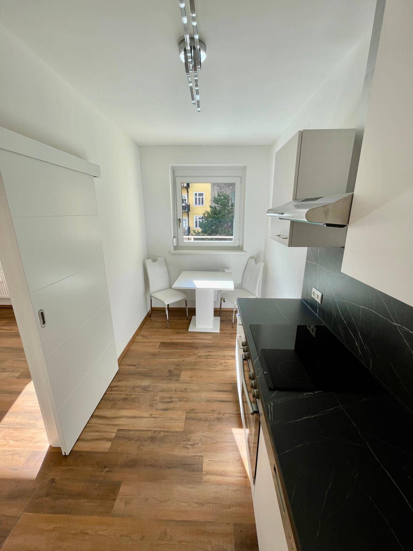 Moderne Küche mit schwarzer Arbeitsplatte, weißen Schränken und kleinem Essbereich am Fenster.