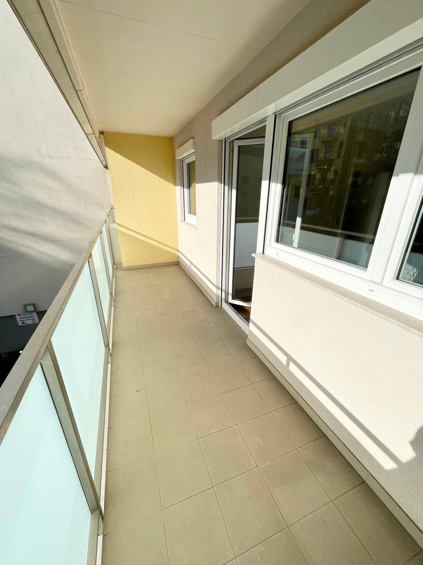 Langer Balkon mit Fliesenboden und Glasgeländer, ideal für entspannte Stunden im Freien.