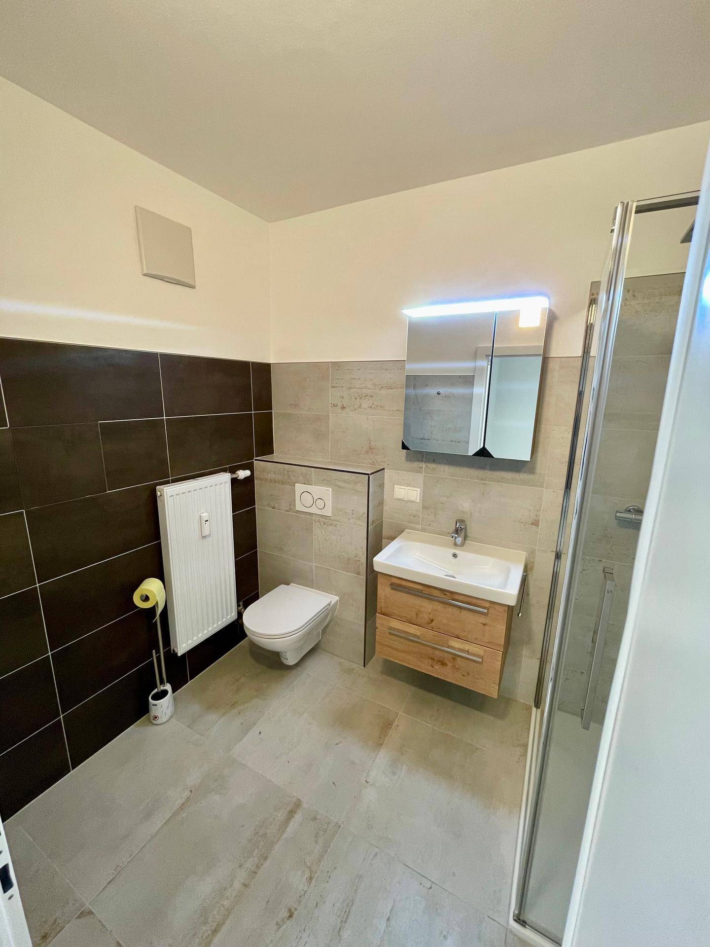 Zeitgemäßes Badezimmer mit WC, Waschtisch und Duschbereich, ausgestattet mit modernen Fliesen.