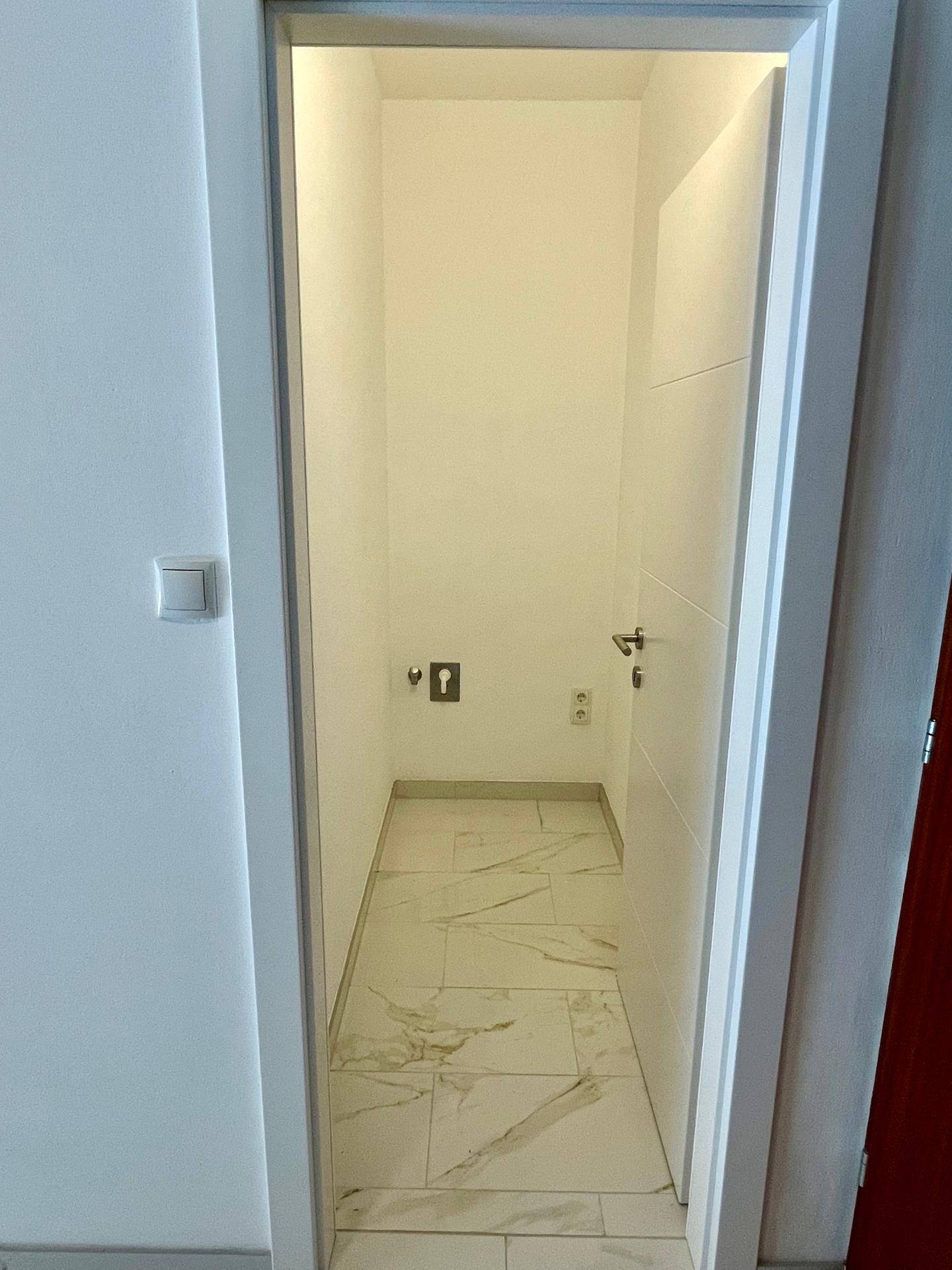 Praktischer Abstellraum mit Fliesenboden, ideal für Waschmaschine oder Lagerung.