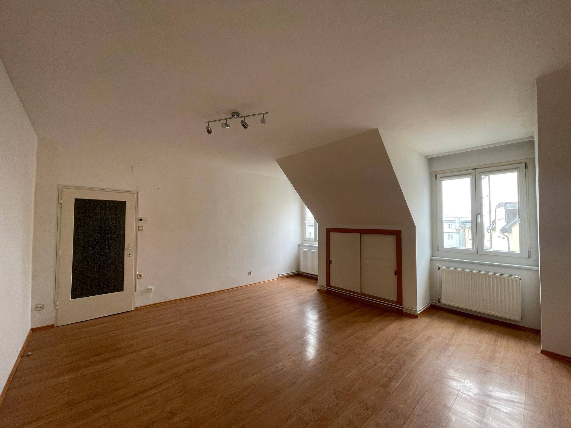 Großes Dachgeschosszimmer mit Holzboden, schrägen Wänden und zwei Fenstern, bietet viel Tageslicht.