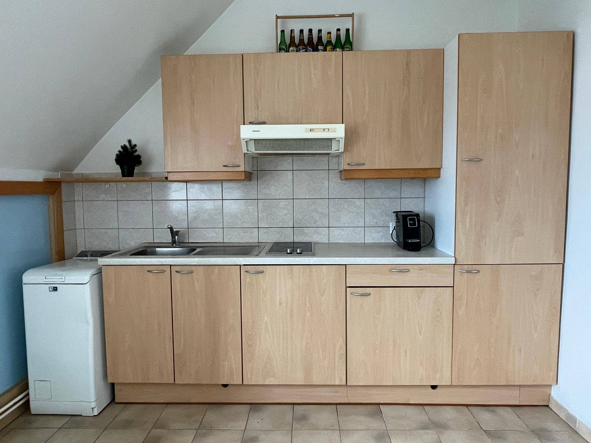 Einbauküche mit hellen Holzfronten, Fliesenboden und grundlegenden Küchengeräten.
