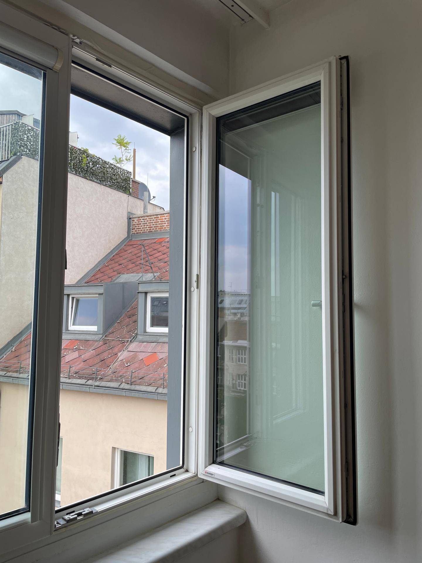 Offenes Fenster mit Blick auf die städtische Umgebung und die Dächer der Nachbargebäude.