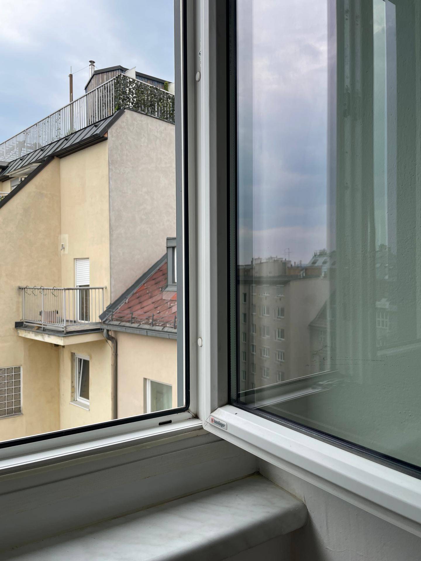 Blick aus dem Fenster auf die umliegenden Gebäude und einen Balkon im Hintergrund.