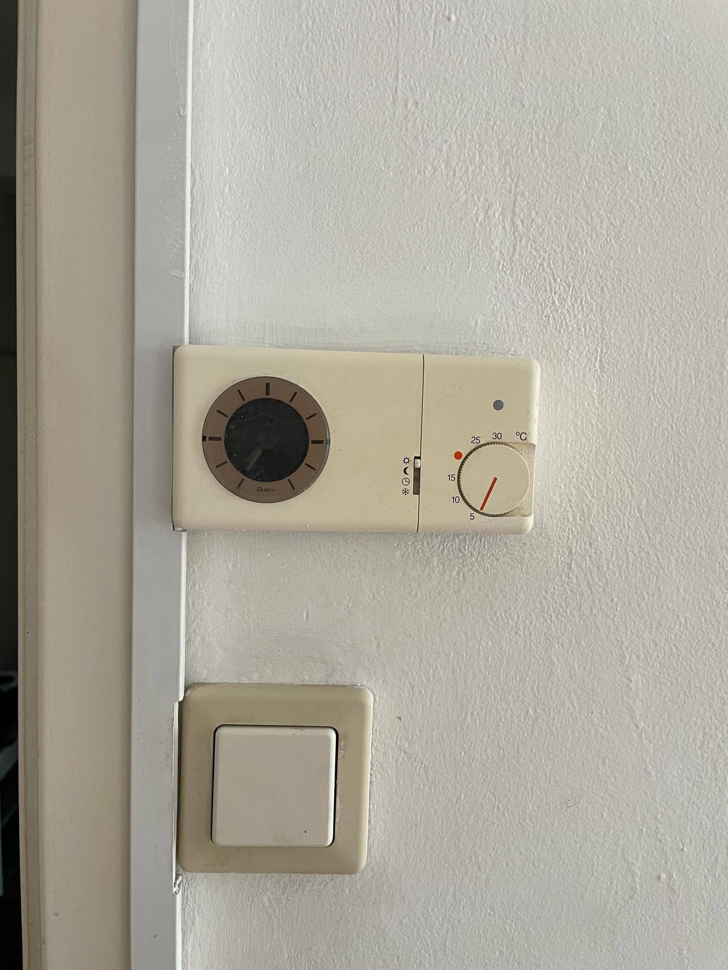 Wandthermostat und Lichtschalter an einer weißen Wand, zeigt die Steuerungselemente.