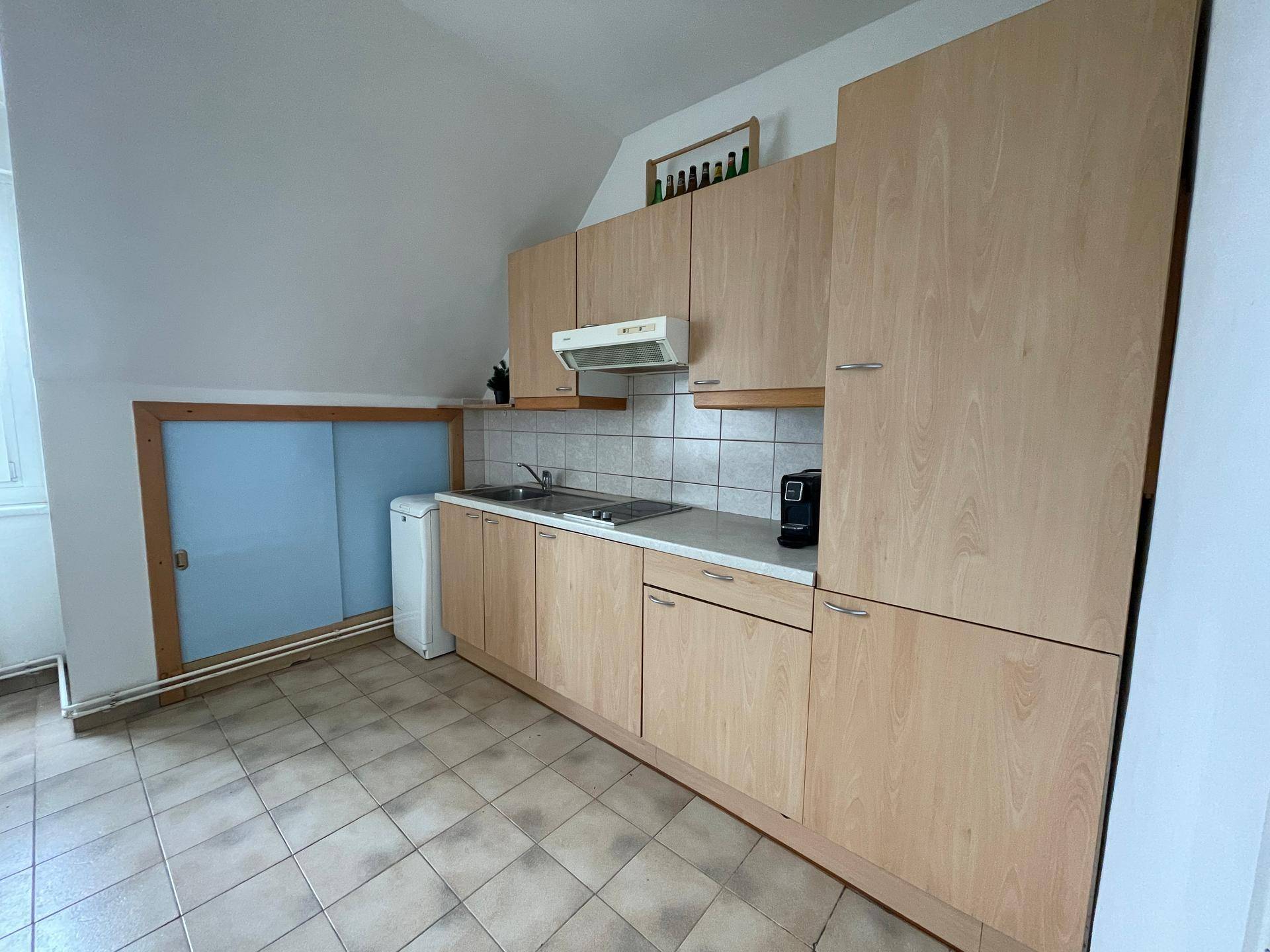Küche im Dachgeschoss mit Holzschränken, Fliesenboden und integrierten Geräten unter der Schräge.