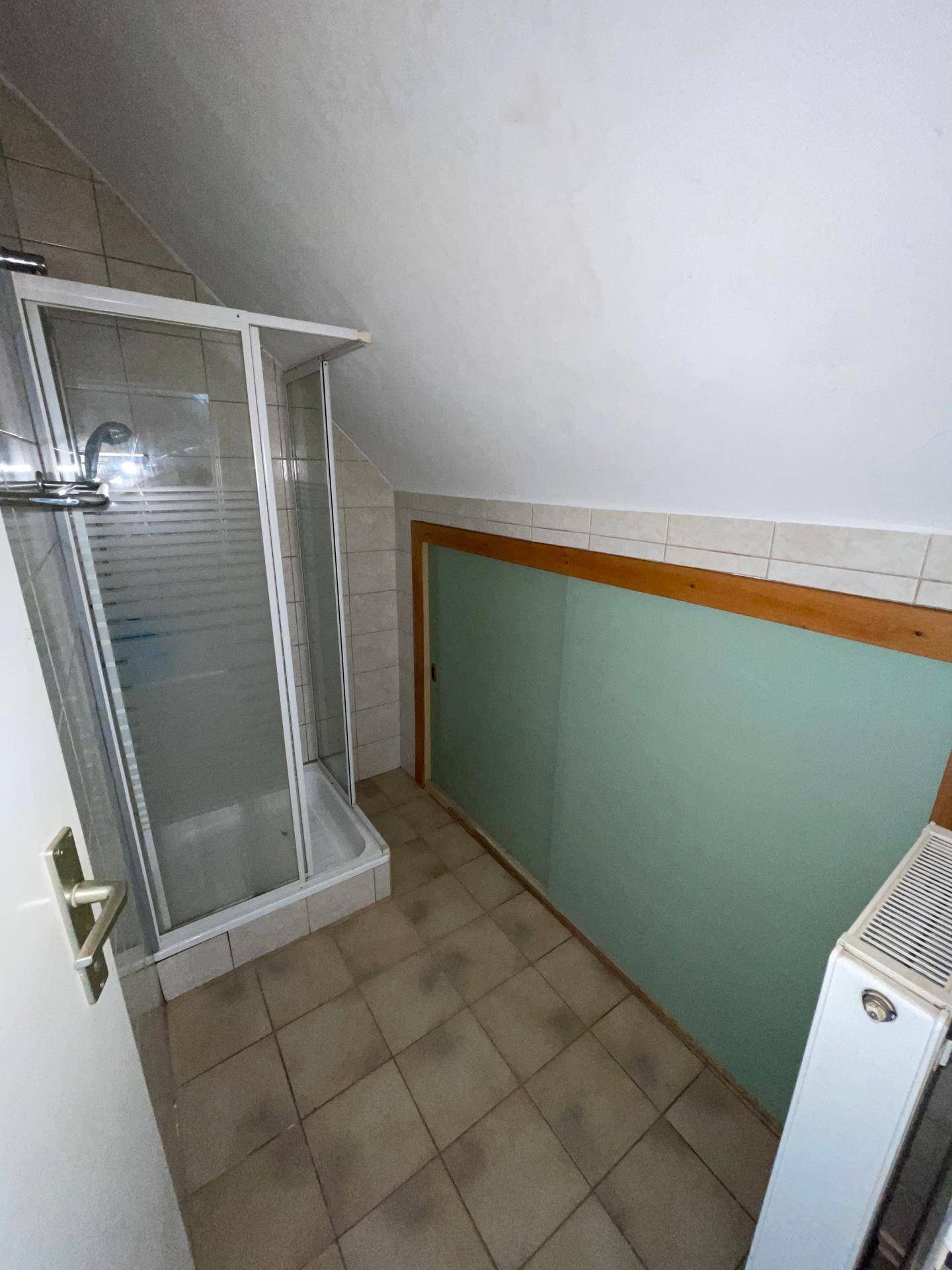 Badezimmer mit Duschkabine, Fliesenboden und schrägen Wänden im Dachgeschoss.