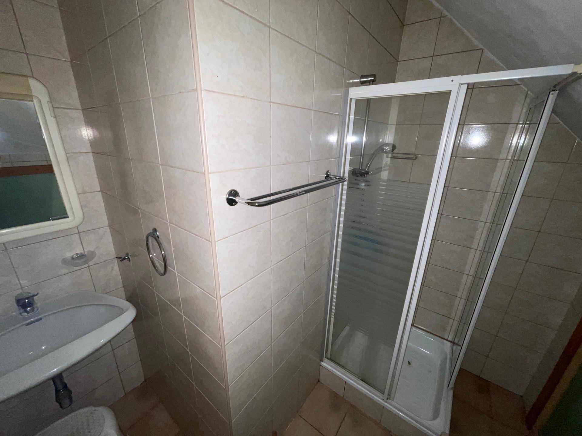 Badezimmer mit Duschkabine, Waschbecken und hellen Fliesen, bietet grundlegenden Komfort.