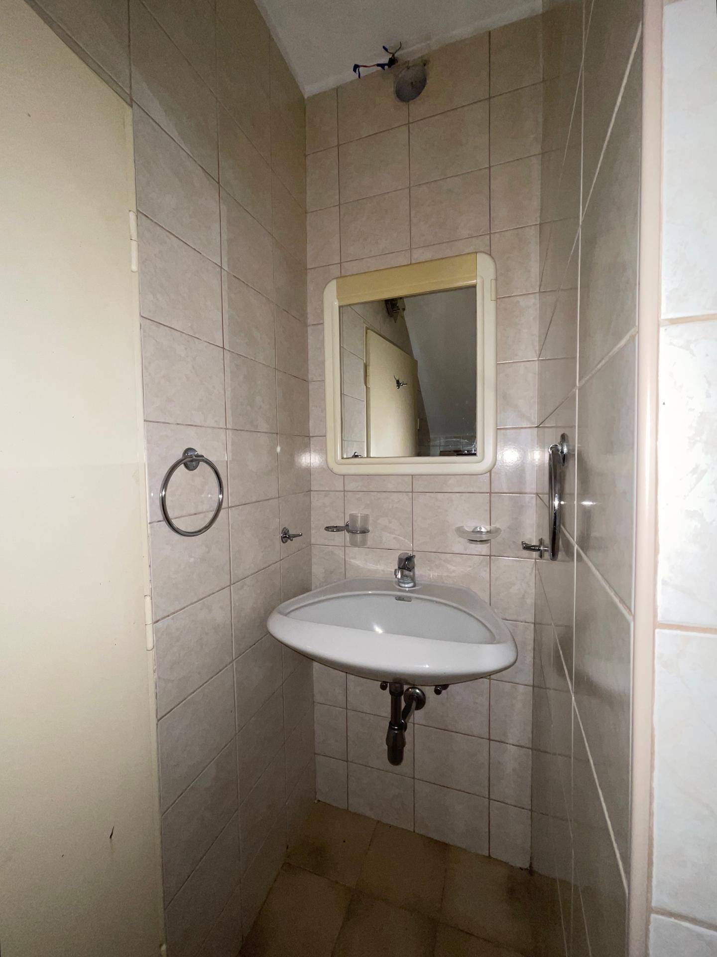 Kleines Badezimmer mit Waschbecken, Spiegel und hellen Fliesen, funktional und kompakt.