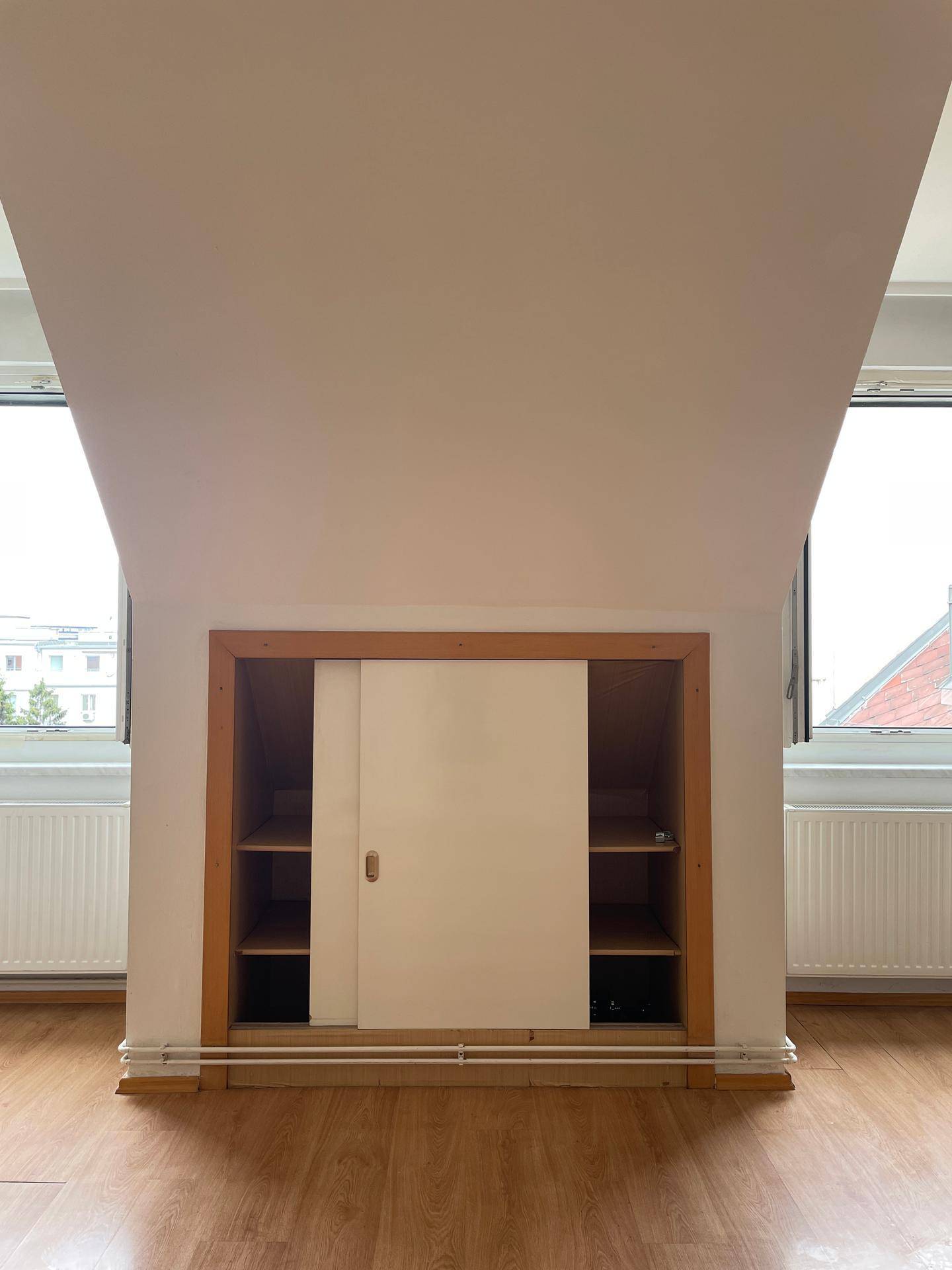 Integriertes Stauraum unter der Dachschräge mit Schiebetüren und Regalen, umgeben von Fenstern.