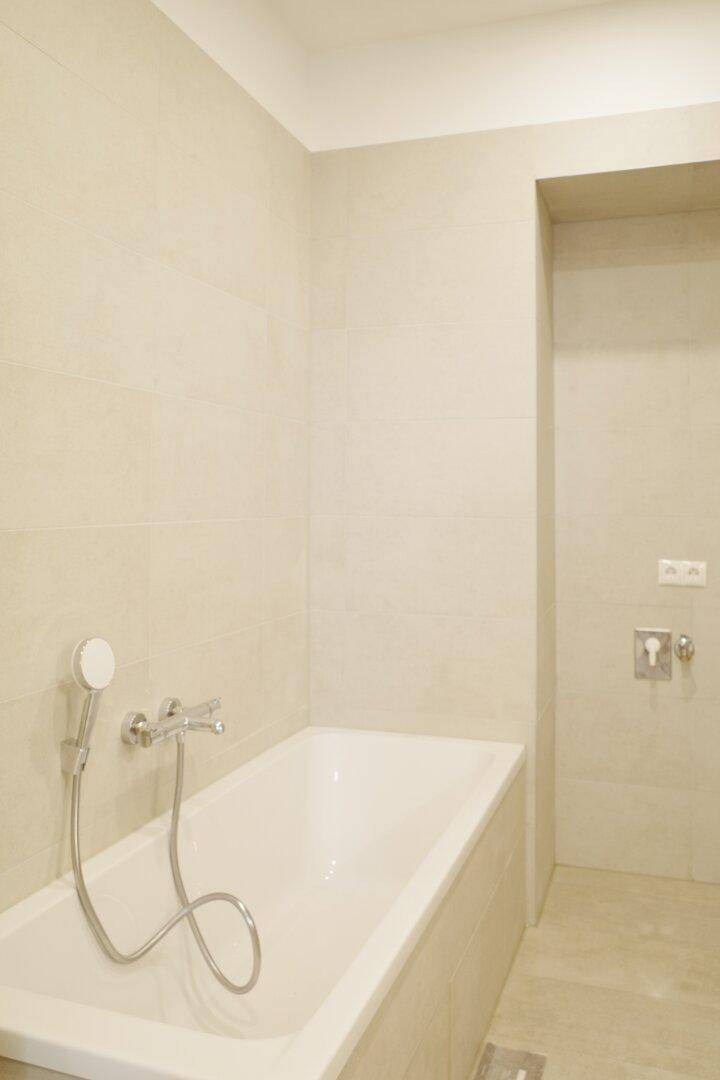 Modernes Badezimmer mit heller Fliesenverkleidung und integrierter Badewanne.