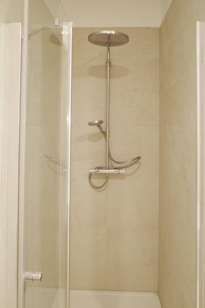 Duschbereich in einem modernen Badezimmer mit Regendusche und hellen Fliesen.