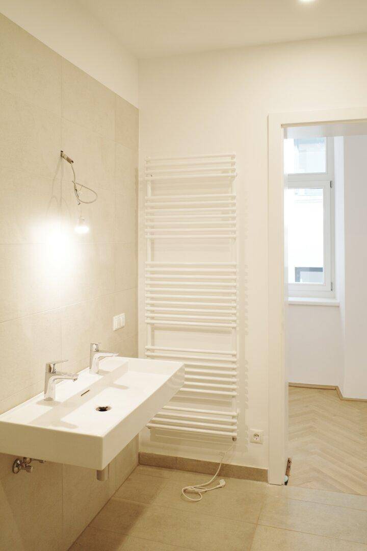 Badezimmer mit Doppelwaschbecken, beheiztem Handtuchhalter und Fensterzugang.