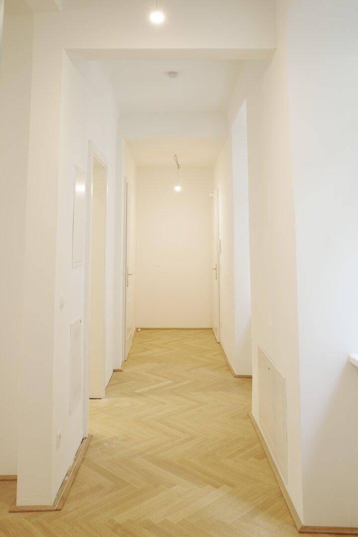 Heller Flur mit Fischgrätparkett und weißen Wänden, der zu weiteren Räumen führt.