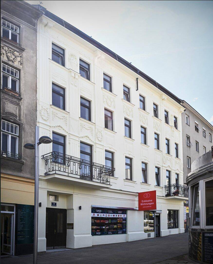 Historische Fassade eines Mehrfamilienhauses mit Balkonen und Geschäften im Erdgeschoss.