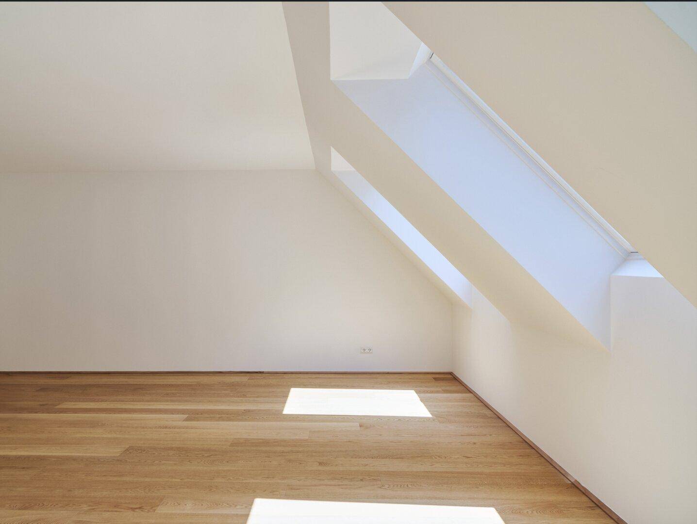 Lichtdurchflutetes Dachgeschosszimmer mit schrägen Wänden und hochwertigem Holzboden.