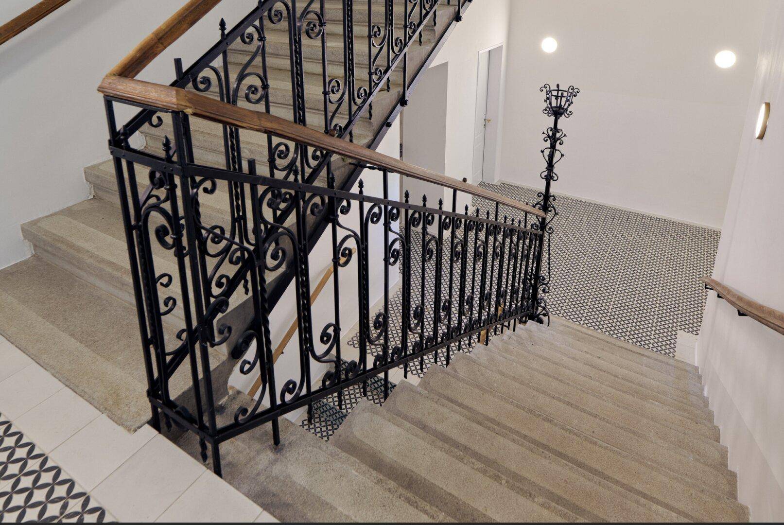 Elegantes Treppenhaus mit schmiedeeisernem Geländer und gemusterten Fliesen im Eingangsbereich.