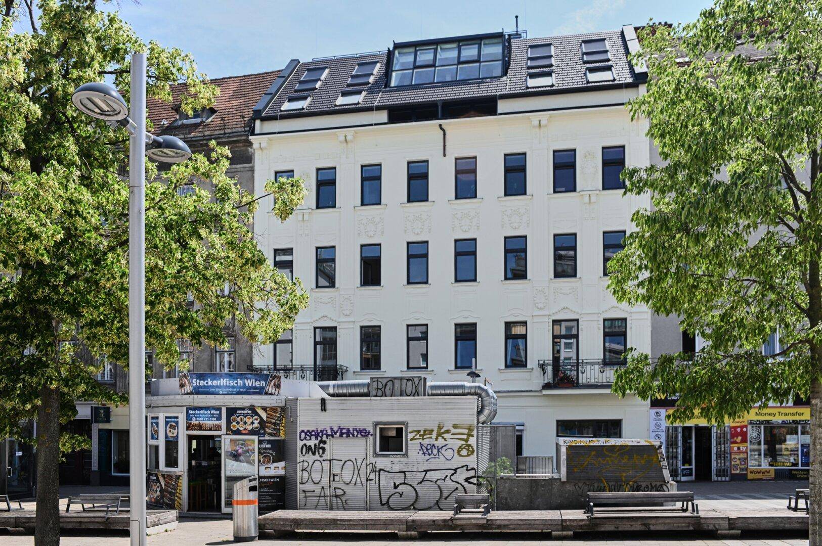 Mehrstöckiges Wohngebäude mit klassischer Fassade und modernem Dachgeschossausbau in urbaner Umgebung.