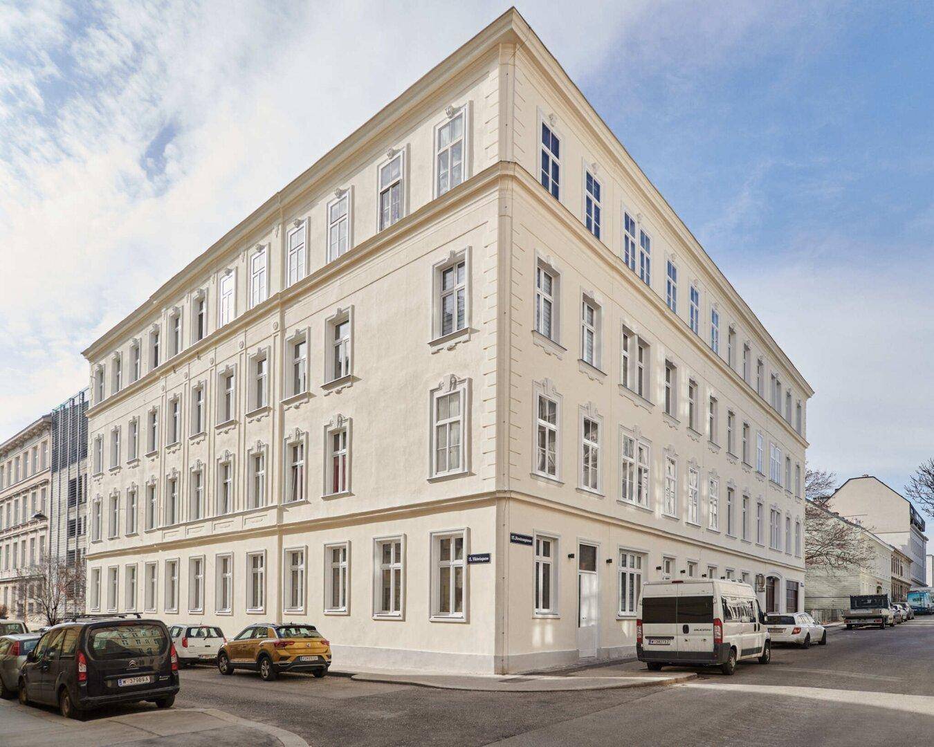 Historisches Eckgebäude mit klassischer Fassade und vielen Fenstern in städtischer Umgebung.