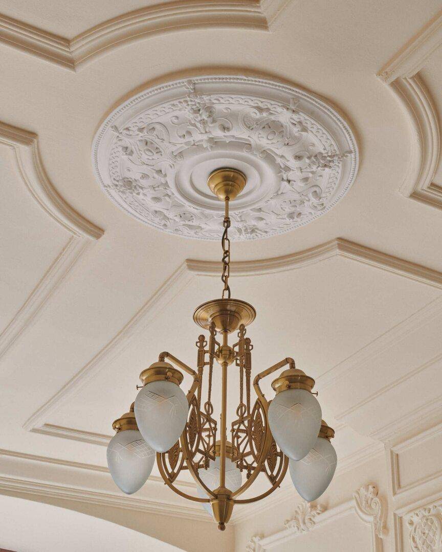 Detailaufnahme einer Stuckdecke mit klassischem Kronleuchter und kunstvollen Zierelementen.