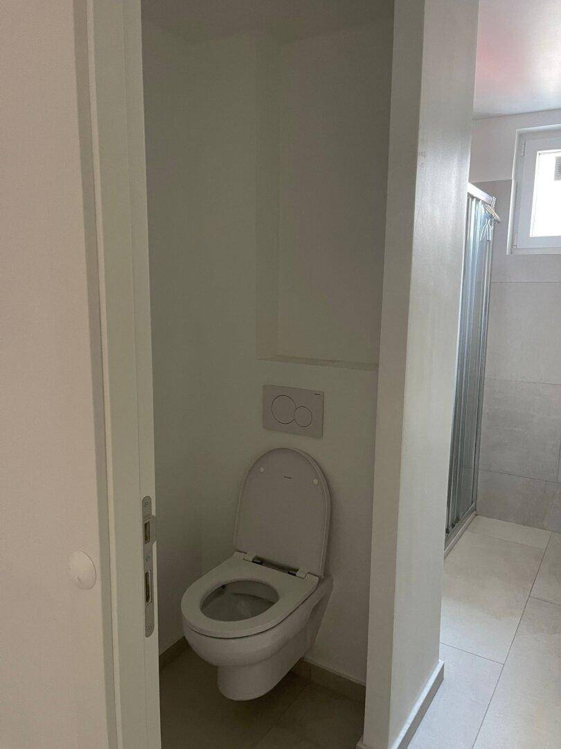 Wandhängendes WC in einem gefliesten Bereich, angrenzend an eine Duschkabine.