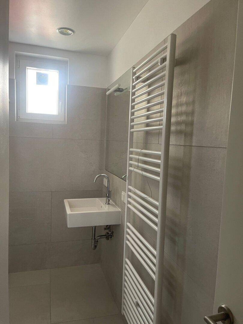 Modernes Badezimmer mit Waschbecken, Spiegel, beheiztem Handtuchhalter und Fenster für Tageslicht.