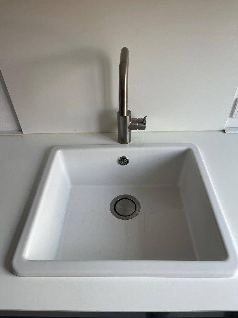 Nahaufnahme eines weißen Spülbeckens mit modernem, hohem Wasserhahn in der Küche.