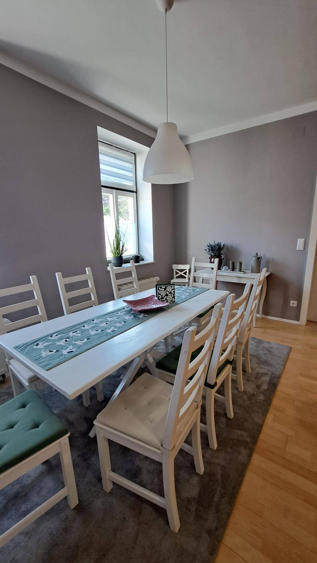 Geräumiger Essbereich mit großem weißen Tisch, Stühlen und zwei Fenstern für viel Licht.