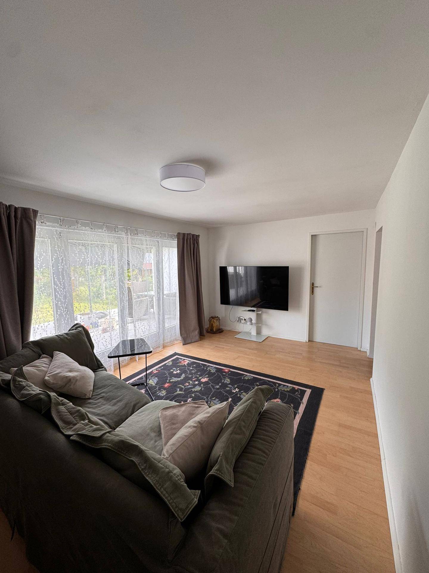 Wohnzimmer mit Sofa, Fernseher und Blick auf den Außenbereich.