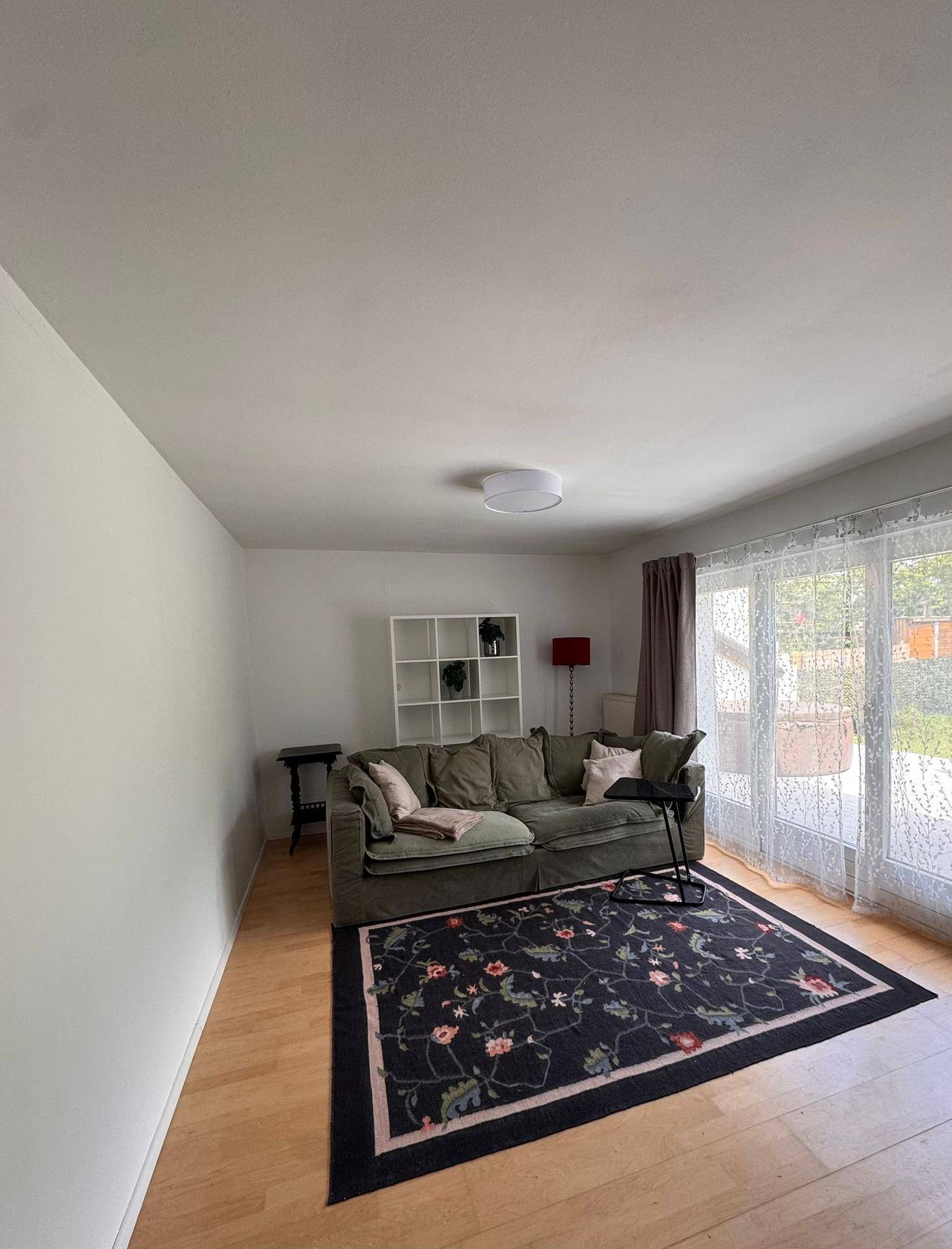 Helles Wohnzimmer mit Sofa, Teppich und Zugang zur Terrasse durch große Fenster.