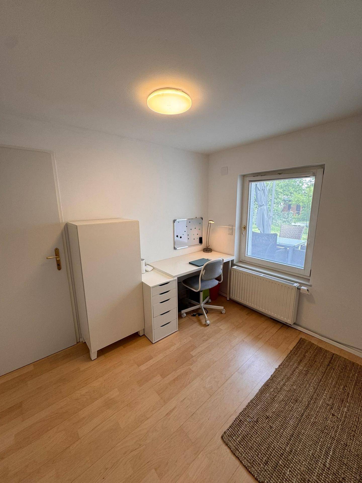 Arbeitszimmer mit Schreibtisch, Bürostuhl und Fenster mit Blick ins Grüne.
