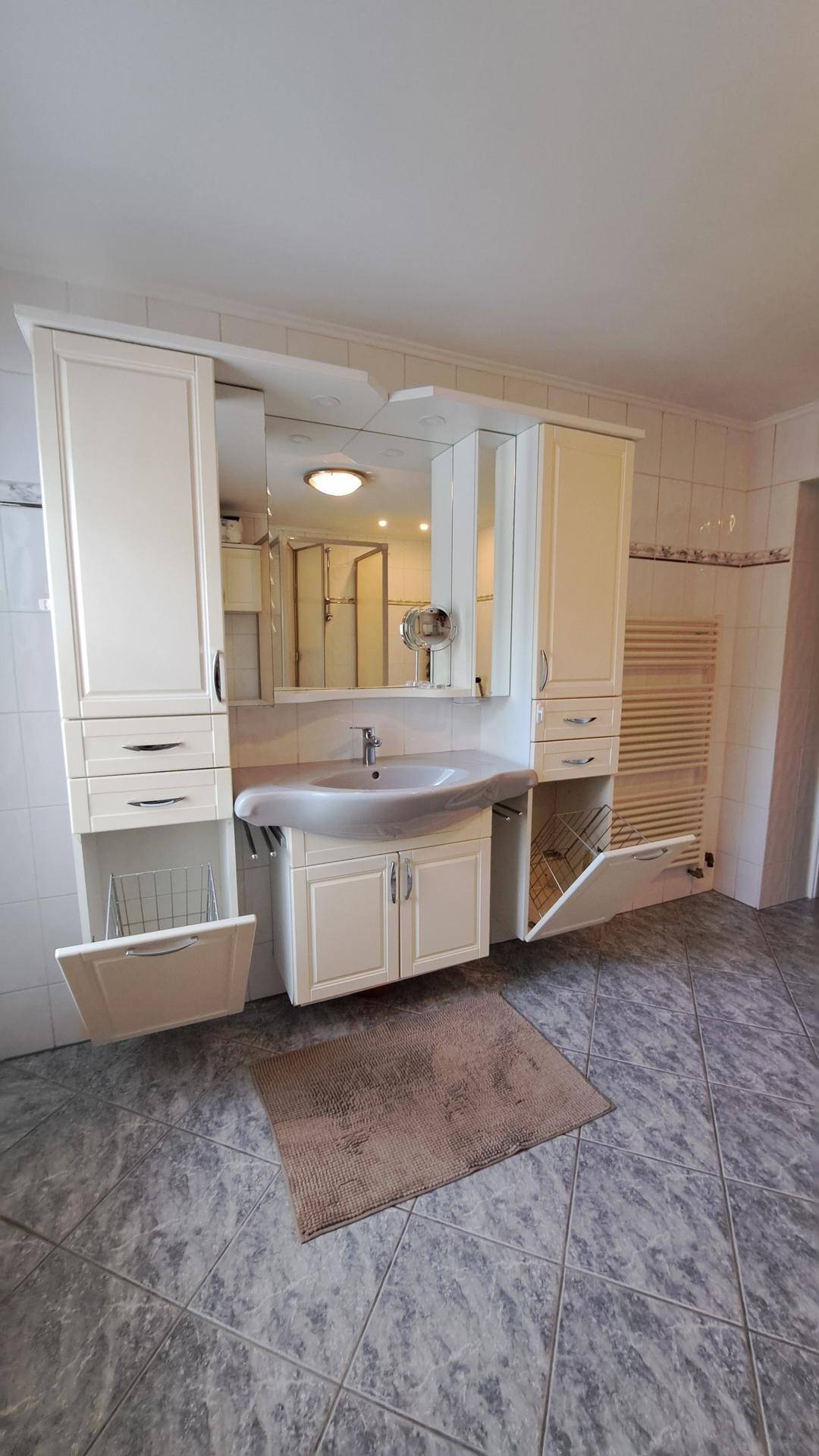 Badezimmer mit Waschtisch, Spiegelschrank und offenem Stauraum.